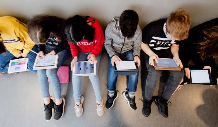 Six children seated successful  a row, utilizing tablets