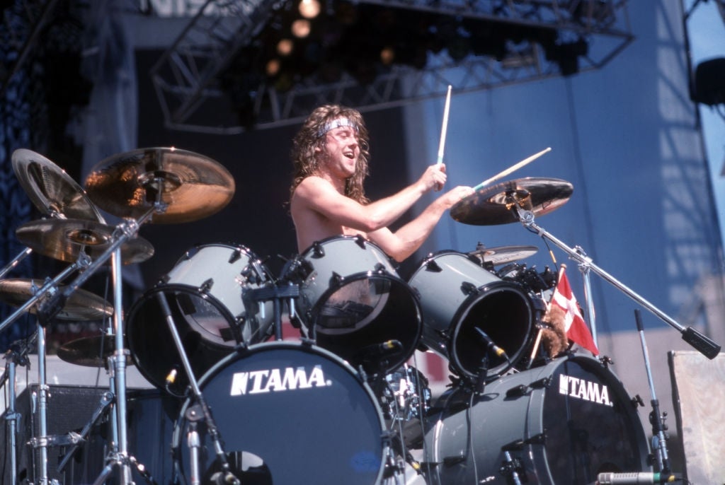 Lars Ulrich playing on a large drum kit during a performance