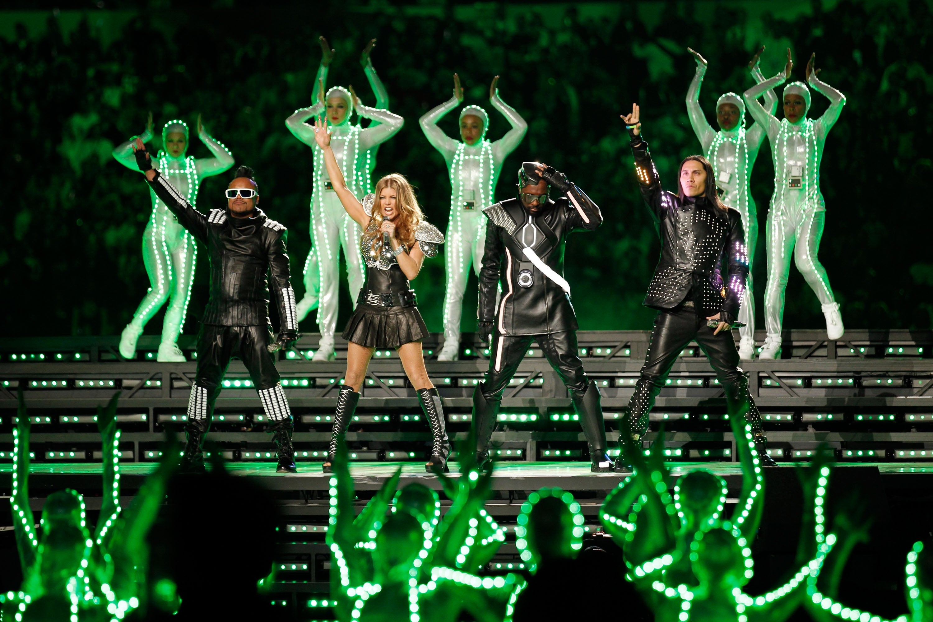 The Black Eyed Peas perform energetically on stage with dancers in futuristic outfits, part of a dynamic music show