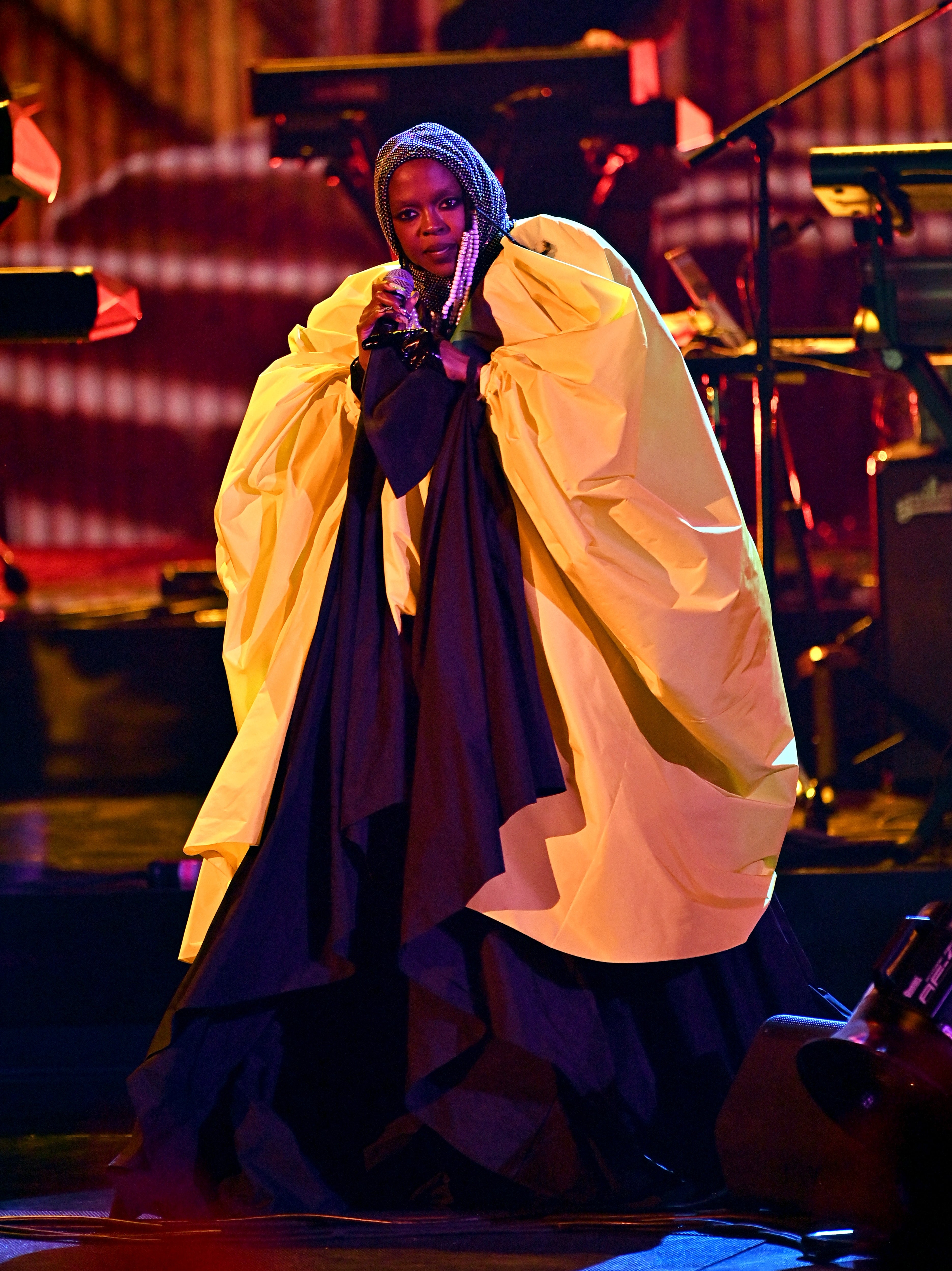 Lauryn Hill on stage in an elegant, flowing outfit with a dramatic, oversized draped gown