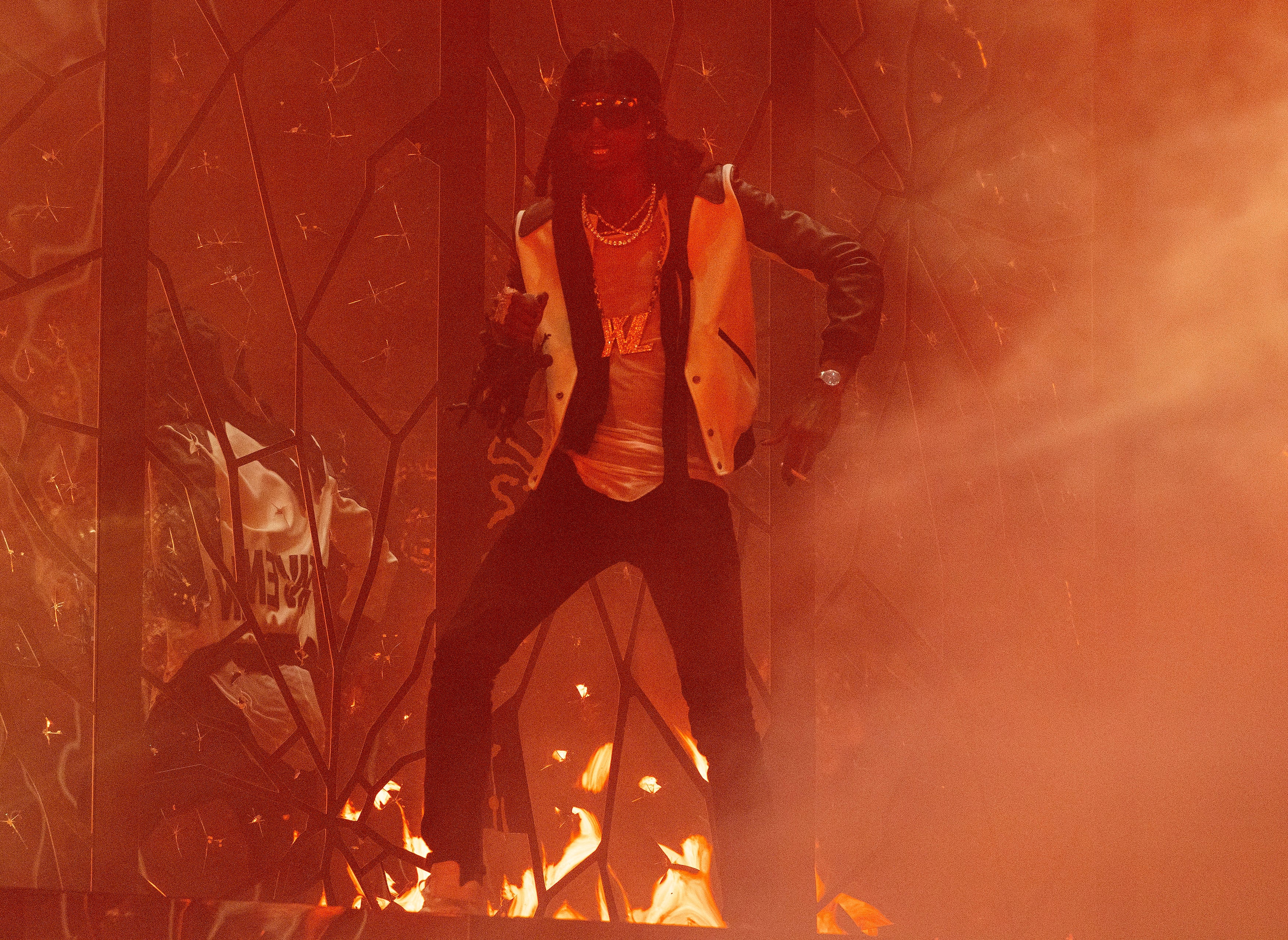 Musician performs energetically on stage with dynamic lighting and smoke effects, wearing a stylish jacket and multiple necklaces