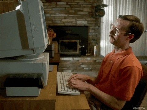 Person in front of an old computer, typing attentively. Retro home setting with a brick fireplace in the background