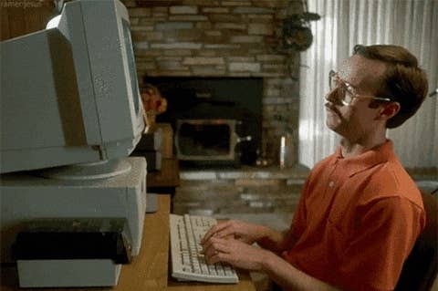 Person in front of an old computer, typing attentively. Retro home setting with a brick fireplace in the background