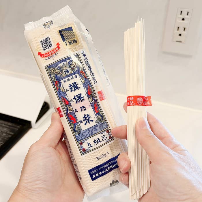 手に持った素麺のパッケージと紐で束ねられた素麺。