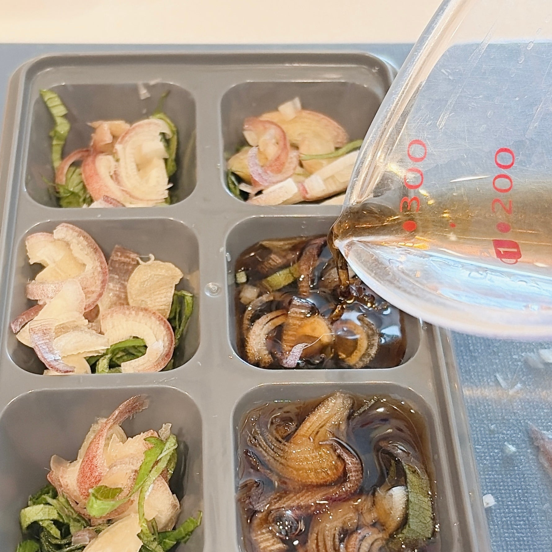 製氷皿に薬味とめんつゆが注がれている様子。