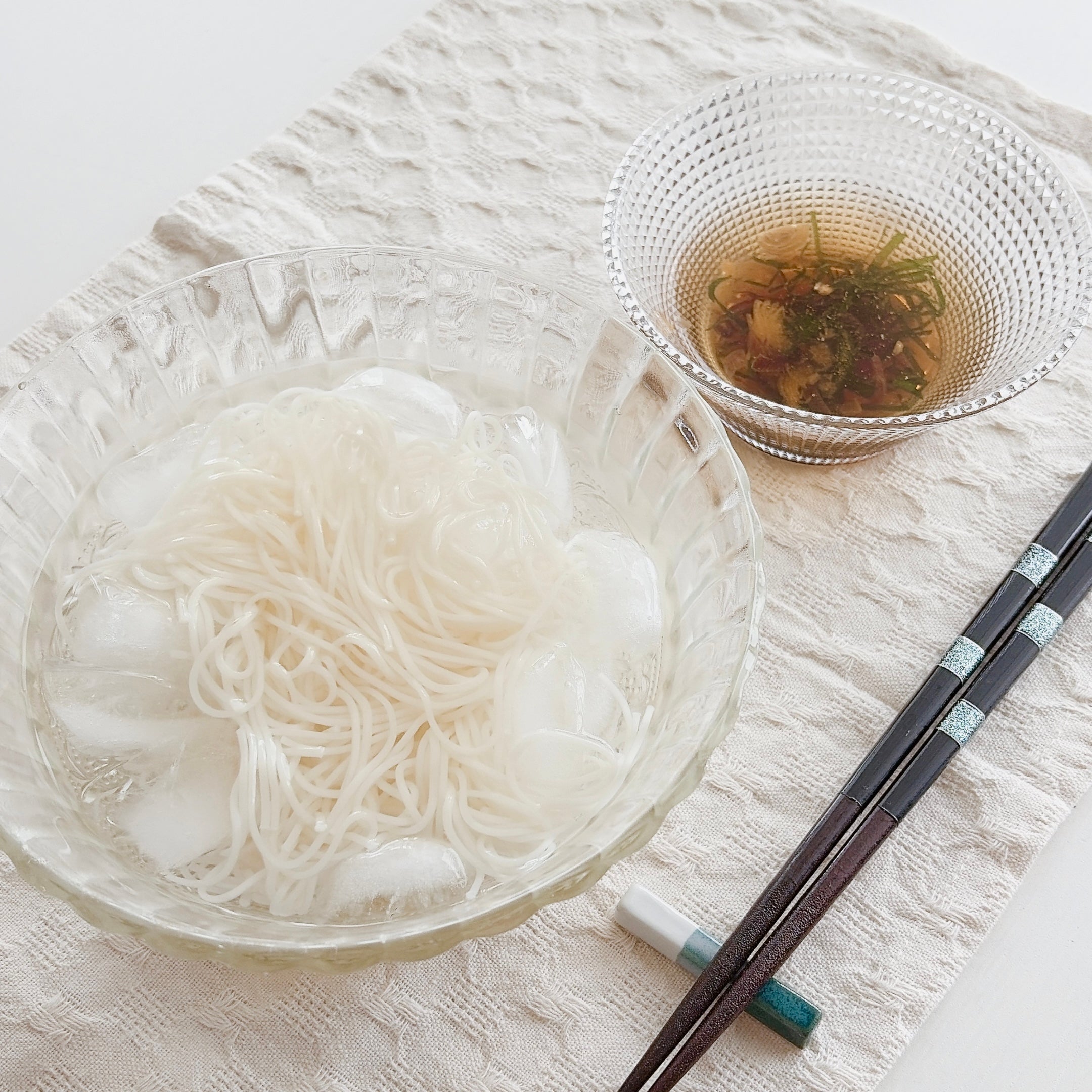 氷水に入ったそうめんとつゆ、箸が置かれたテーブル。シンプルで涼しげな日本の夏の料理。