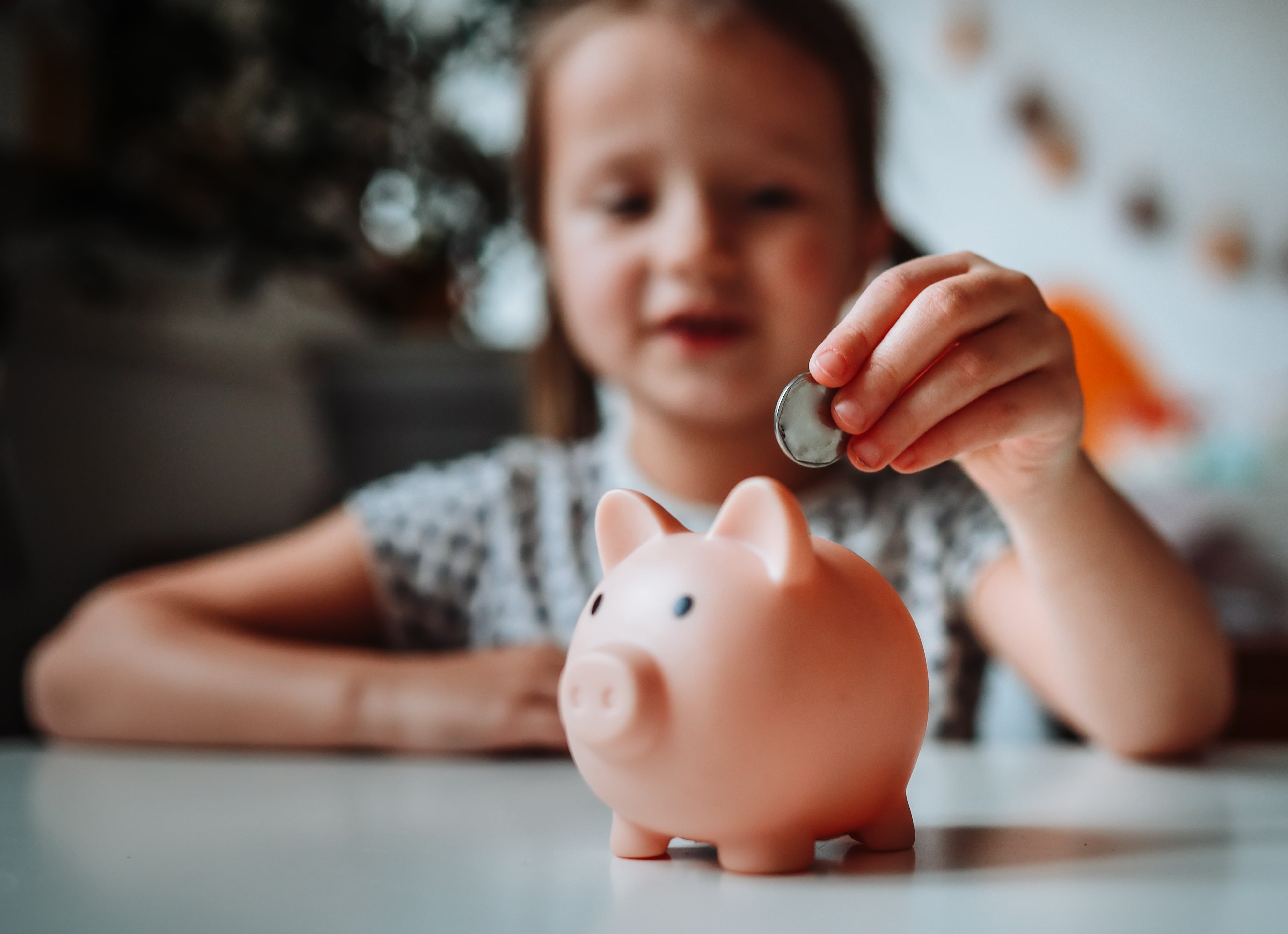 Barn som plasserer en mynt i en sparegris, symboliserer å spare penger og finansiell kompetanse i foreldreskap