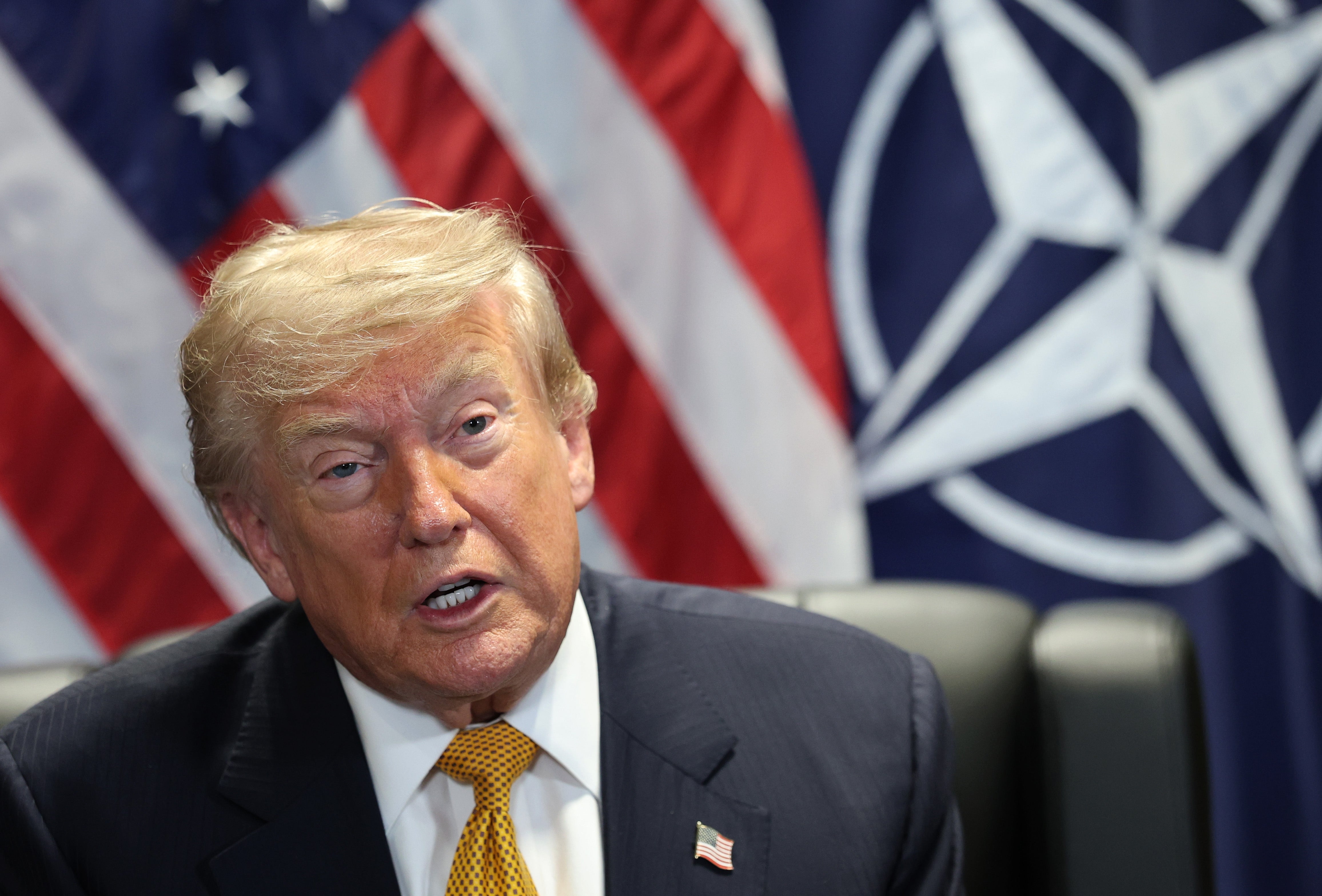 En person i dress snakker foran amerikanske og NATO-flagg på et arrangement