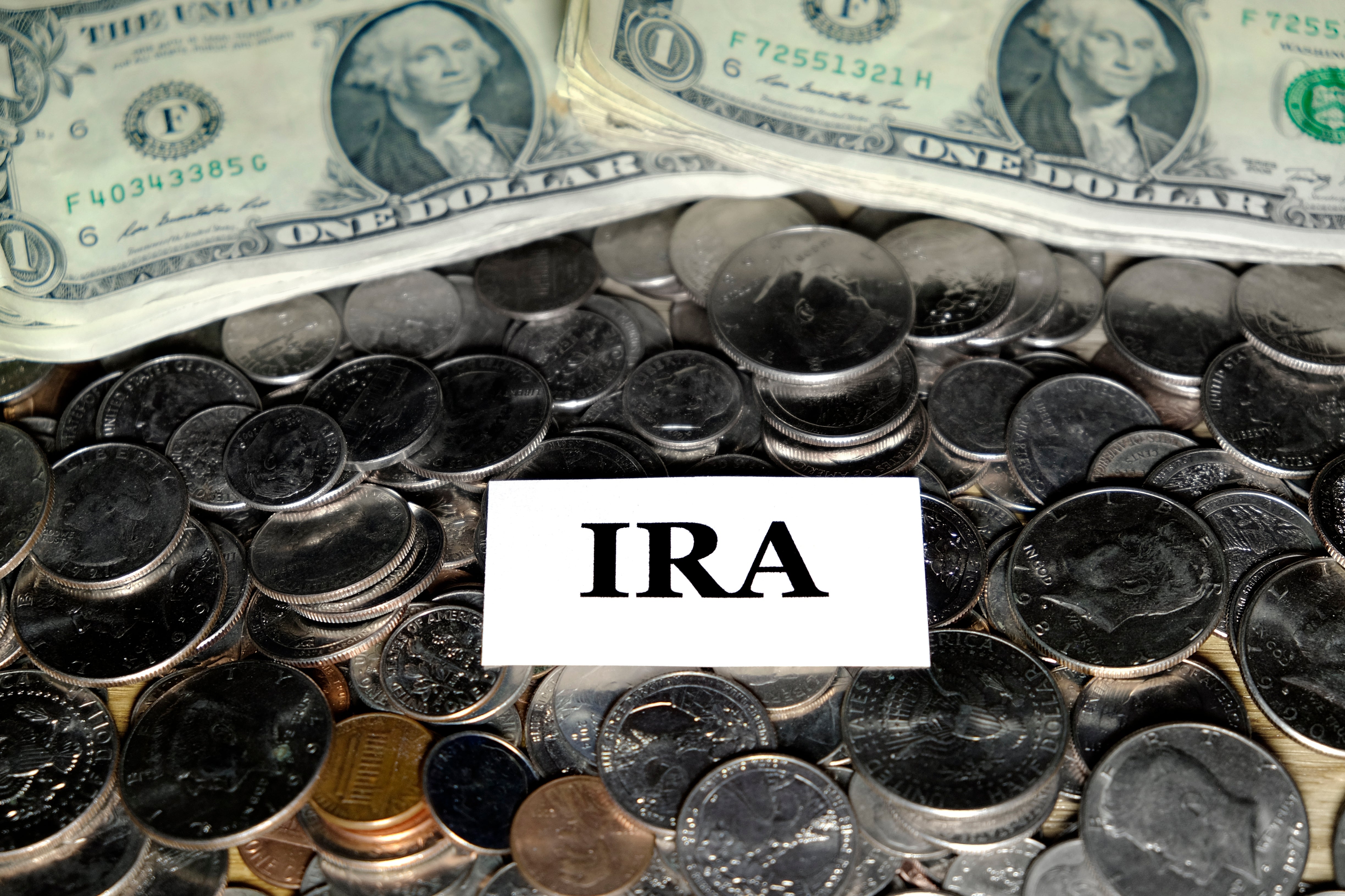 Mynter og dollarsedler rundt et kort med "IRA" trykt på den, som symboliserer spare- eller investeringskontoer