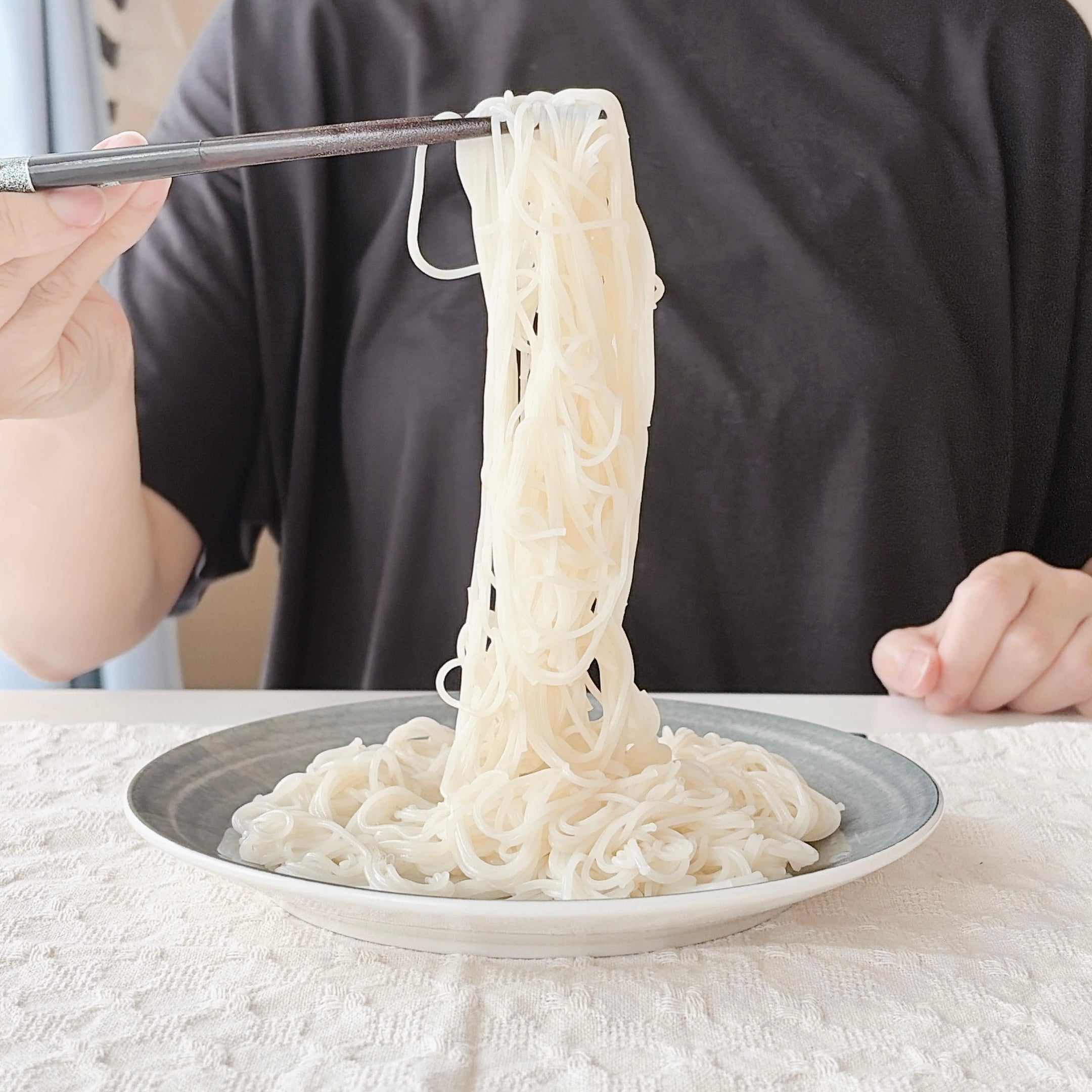 成人女性がそうめんを箸で持ち上げるシーン。