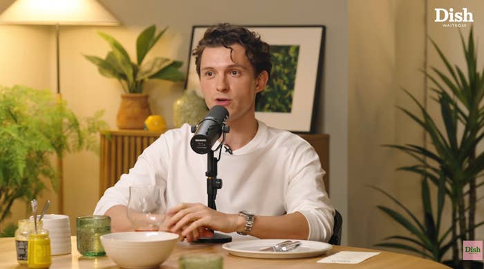 Person seated in front of a microphone at a table with glassware and plants in the background