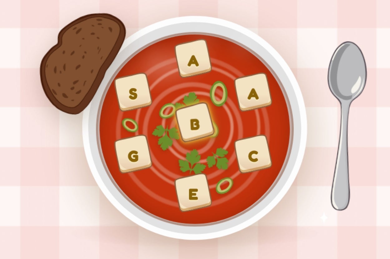 A bowl of tomato soup with letter-shaped crackers spelling "GAMES," garnished with herbs and green onions, next to a slice of bread and a spoon