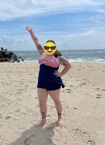 Person at the beach wearing a nautical-style swimsuit with stripes, posing confidently with one arm raised