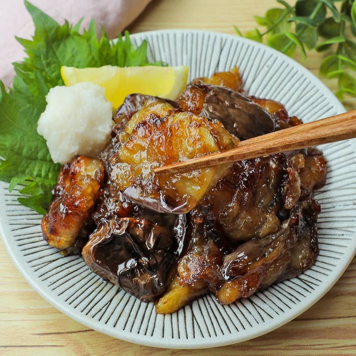 器に盛られた焼き茄子の料理。醤油を絡めたような焼き目がついており、大根おろしとレモンが添えられている。