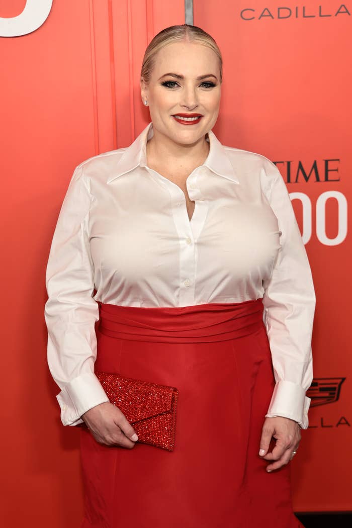 Meghan McCain on red carpet in a sleek blouse and long skirt, holding a glittery clutch, smiling for the camera at a celebrity event