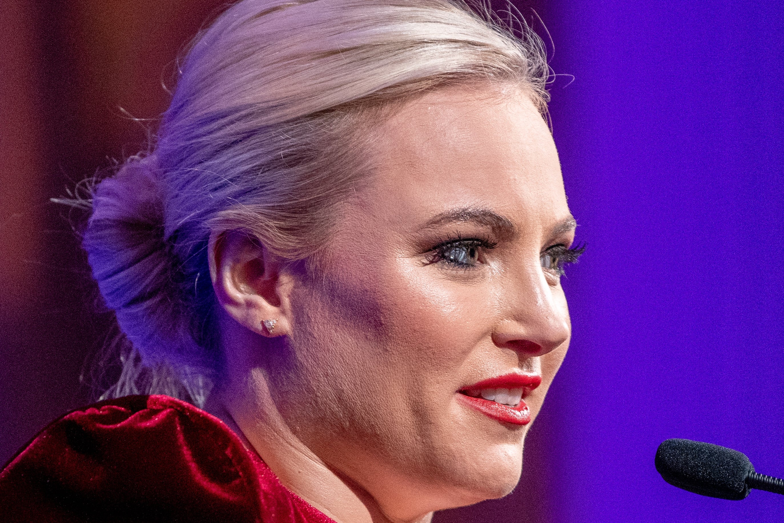 Meghan McCain speaking at a podium, wearing an elegant velvet dress, hair up