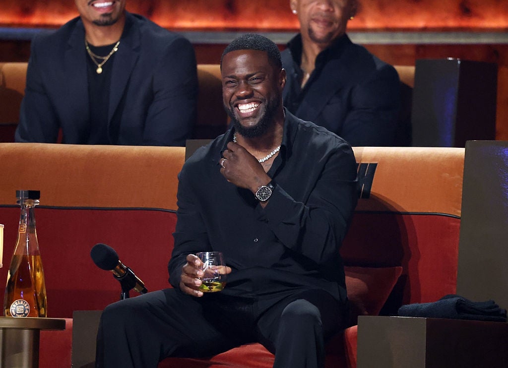 Kevin Hart laughs while sitting with a drink, attending his comedy roast