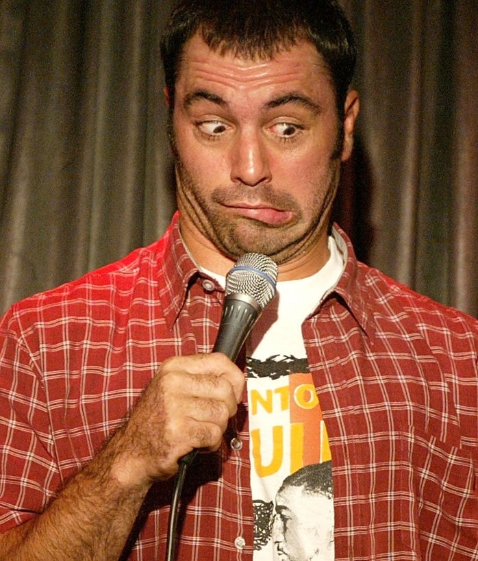 Joe Rogan in the early 2000s holding a microphone while making a humorous face