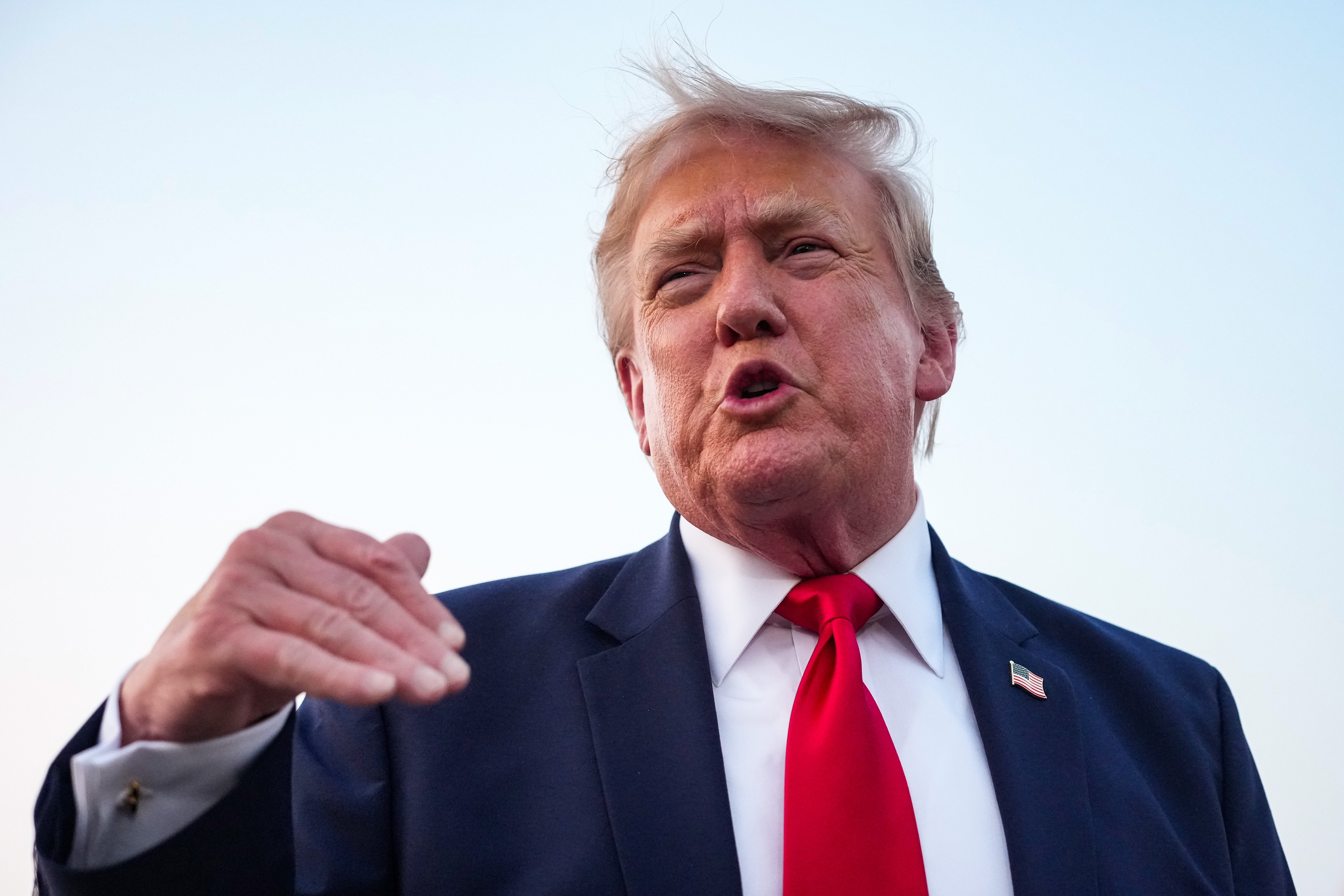 Donald Trump gesturing as he speaks outside with his hair awkwardly blowing in the wind