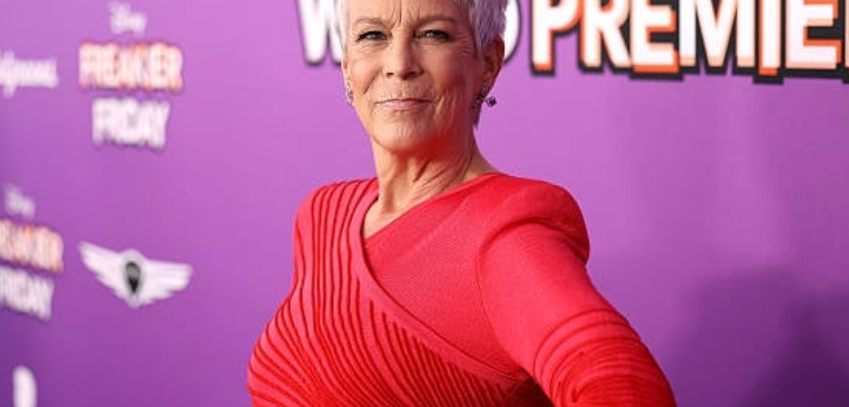 Person in a stylish gown poses confidently at a film premiere event with a vibrant backdrop