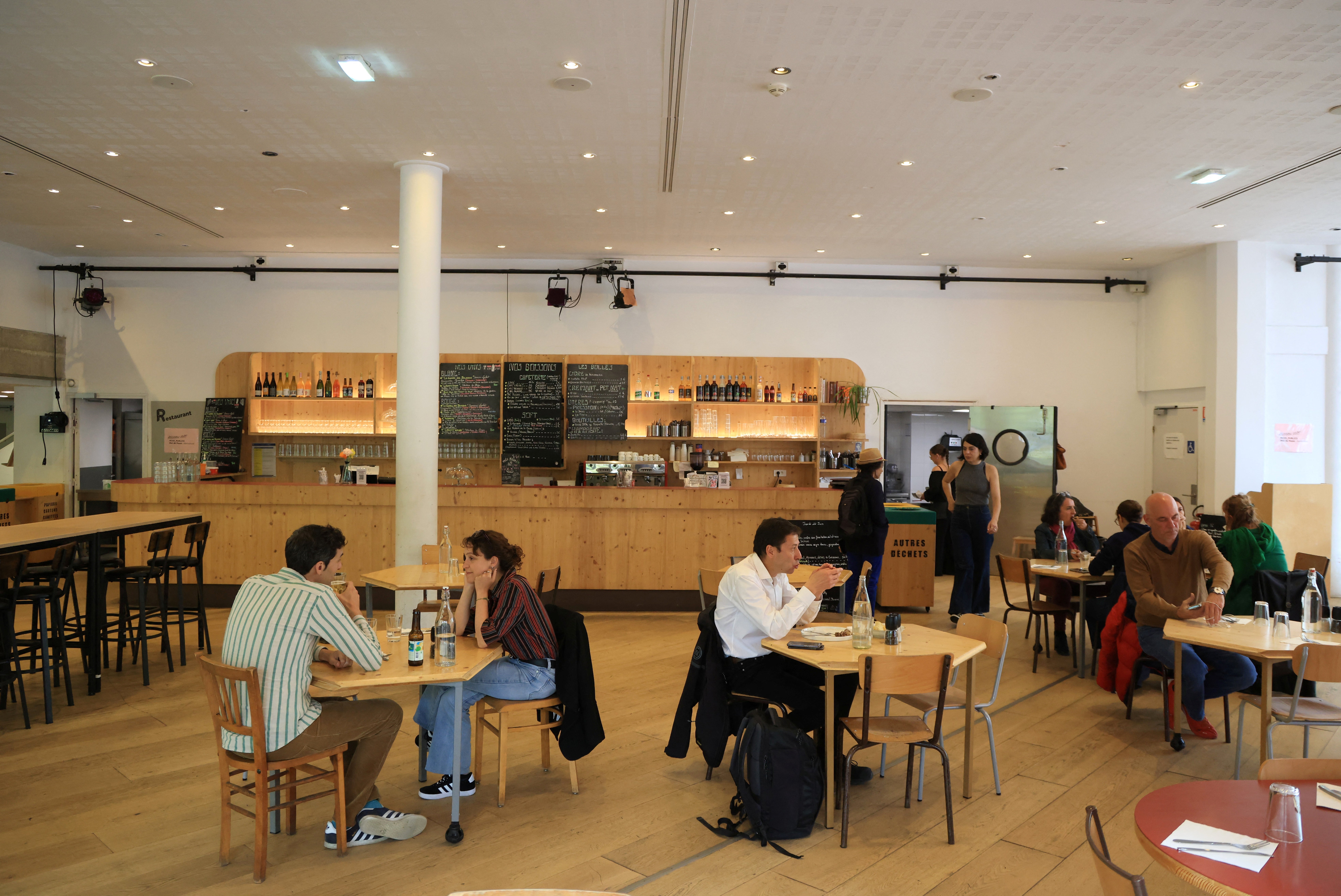 Folk sitter ved bordene på en moderne kafé med en tredisk og tavlemeny i bakgrunnen