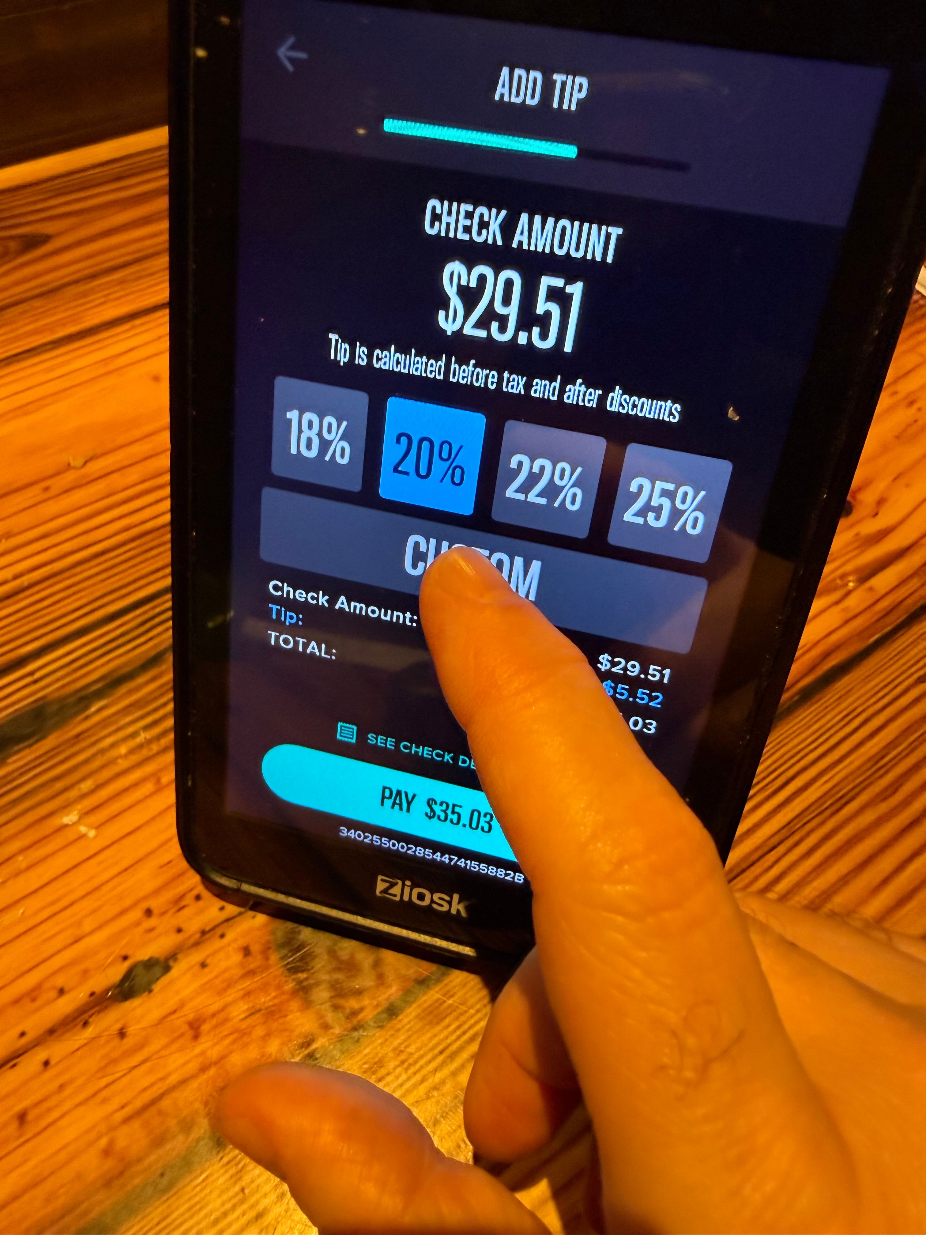 Person som velger et 20 % tips på en berøringsskjermenhet med et sjekkbeløp på $29,51, noe som resulterer i en total betaling på $35,03