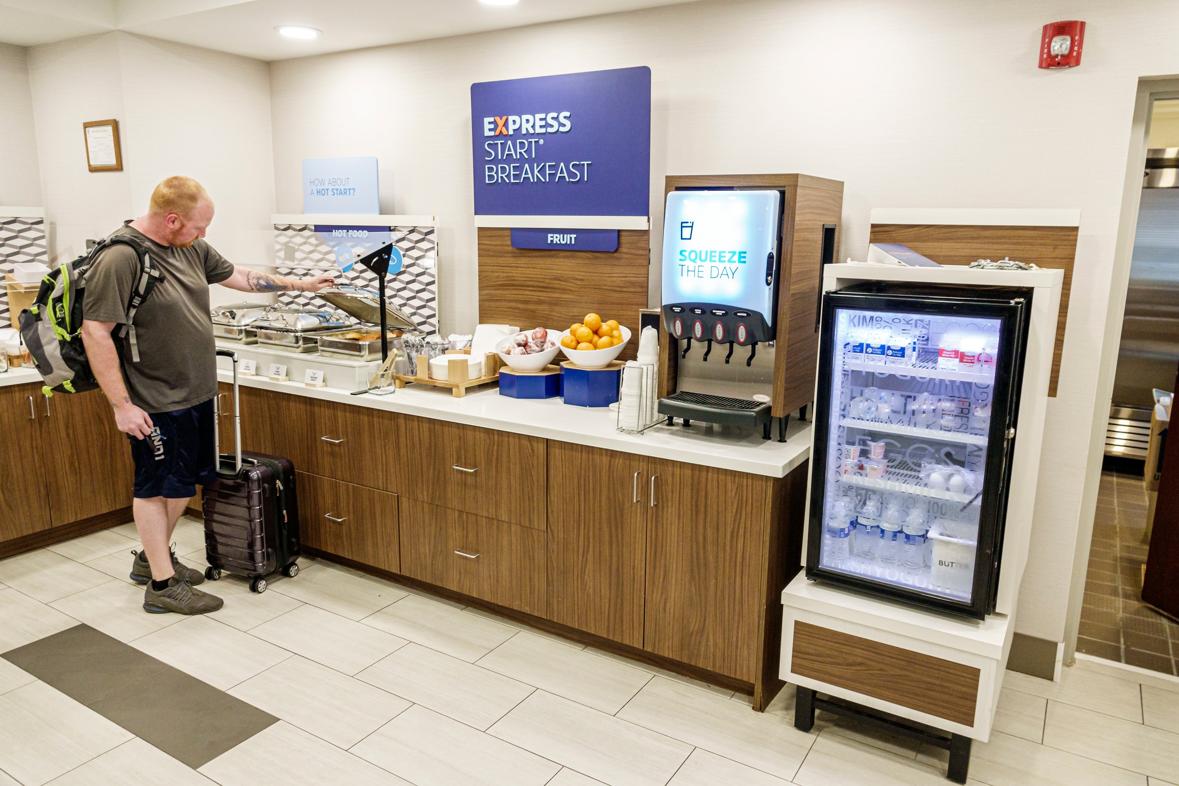 Mannen med en koffert serverer seg selv frokost på en hotellbuffé, med drinker, frukt og bakverk