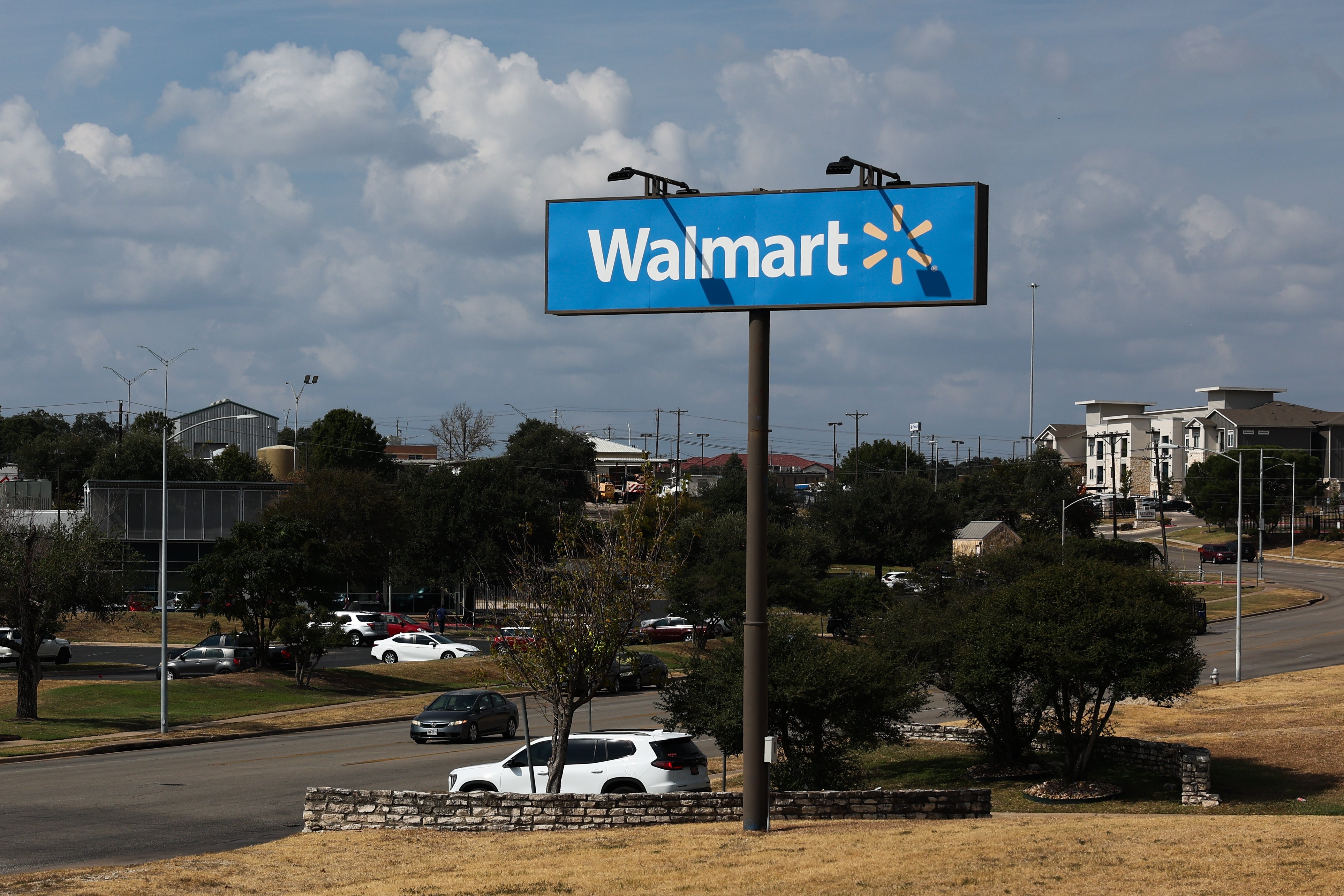 Walmart-skilt på en høy stolpe i et forstadsområde med parkerte biler og bygninger i bakgrunnen