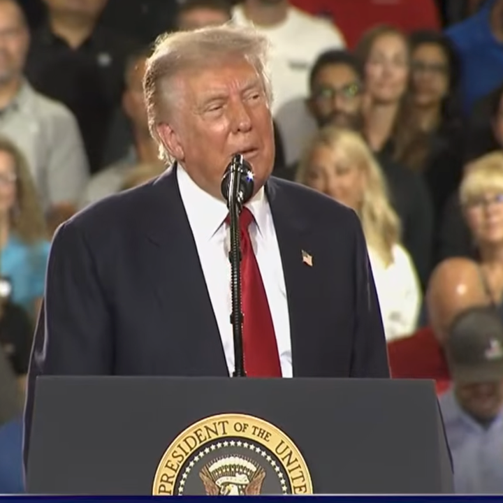 A person speaks at a podium with a presidential seal, addressing an audience at an event