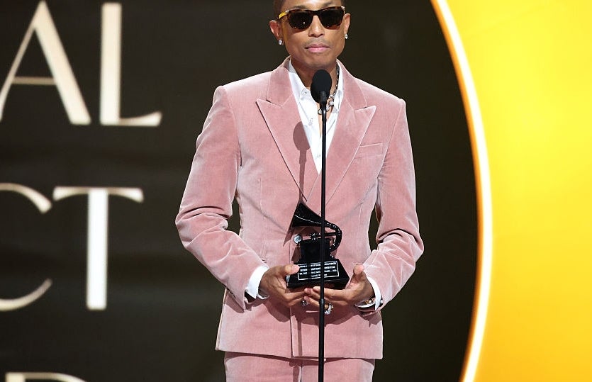 Person in a velvet suit with sunglasses holds a trophy while speaking at an awards ceremony