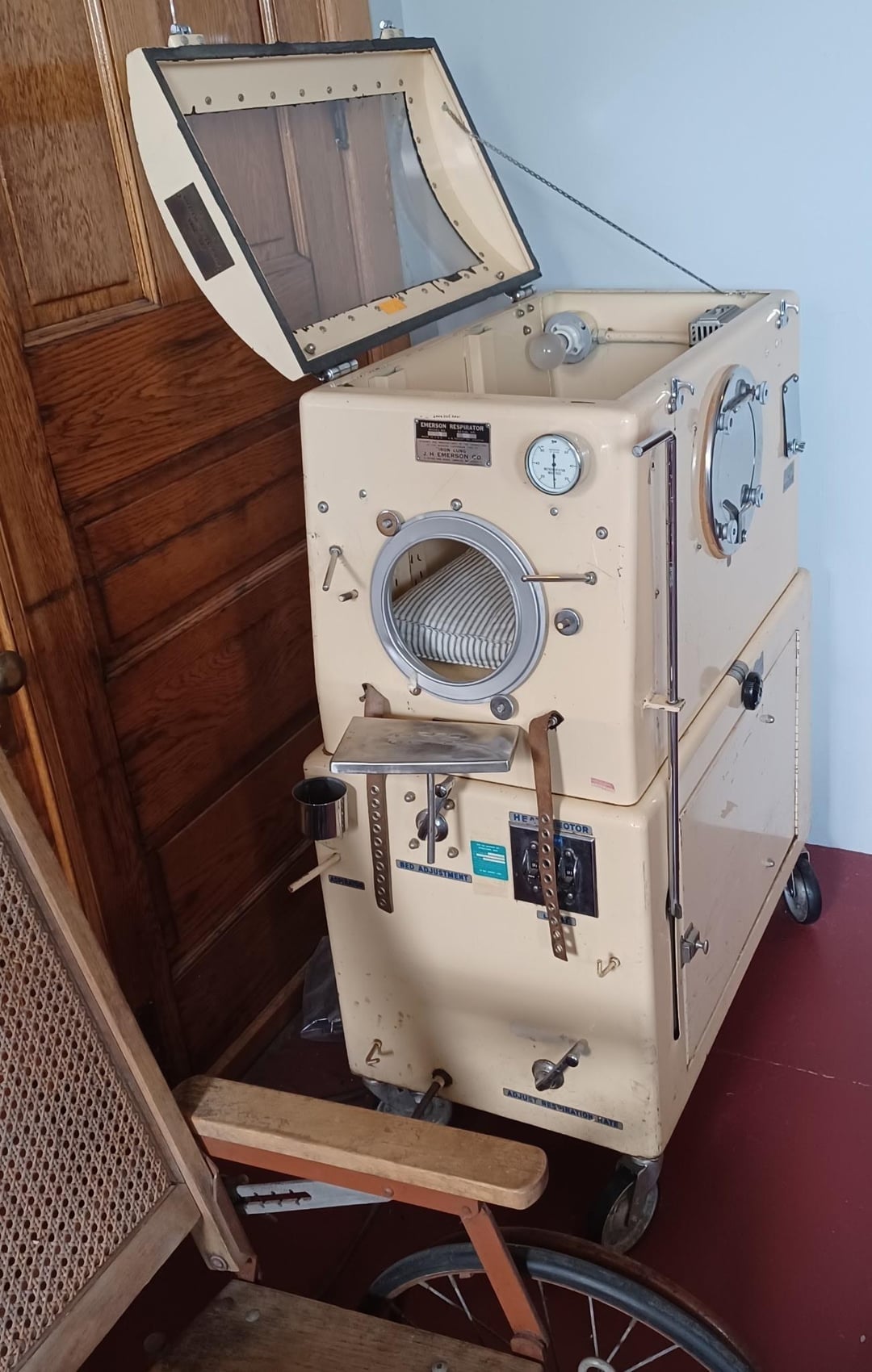 An iron lung machine used for respiratory support, featuring control dials and a metal frame with a soft interior for patient use