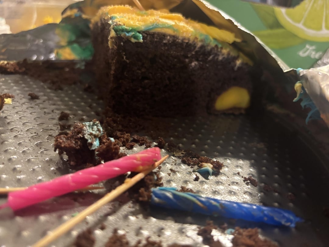 A partially eaten chocolate cake with colorful frosting and two used candles on the side