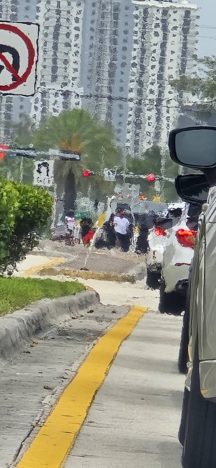 View of busy urban street through car window, showing traffic and pedestrians. Distorted effect suggests heat or rain