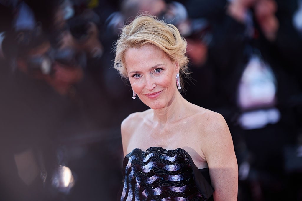 A person on a red carpet event is wearing a strapless dress with a shimmering, textured bodice and drop earrings, smiling at the camera