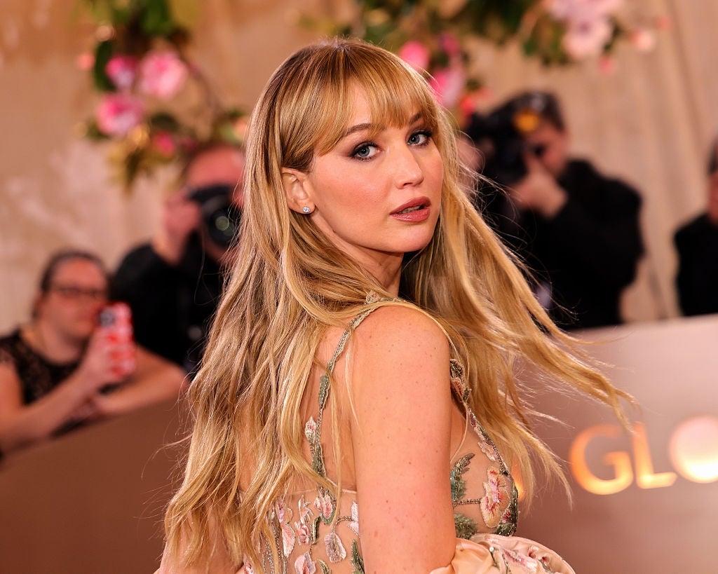 Person on a glamorous event carpet wearing a floral-patterned dress, looking over their shoulder with photographers in the background