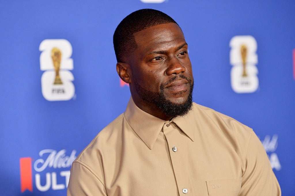 A person in a tan shirt stands against a blue backdrop with logos
