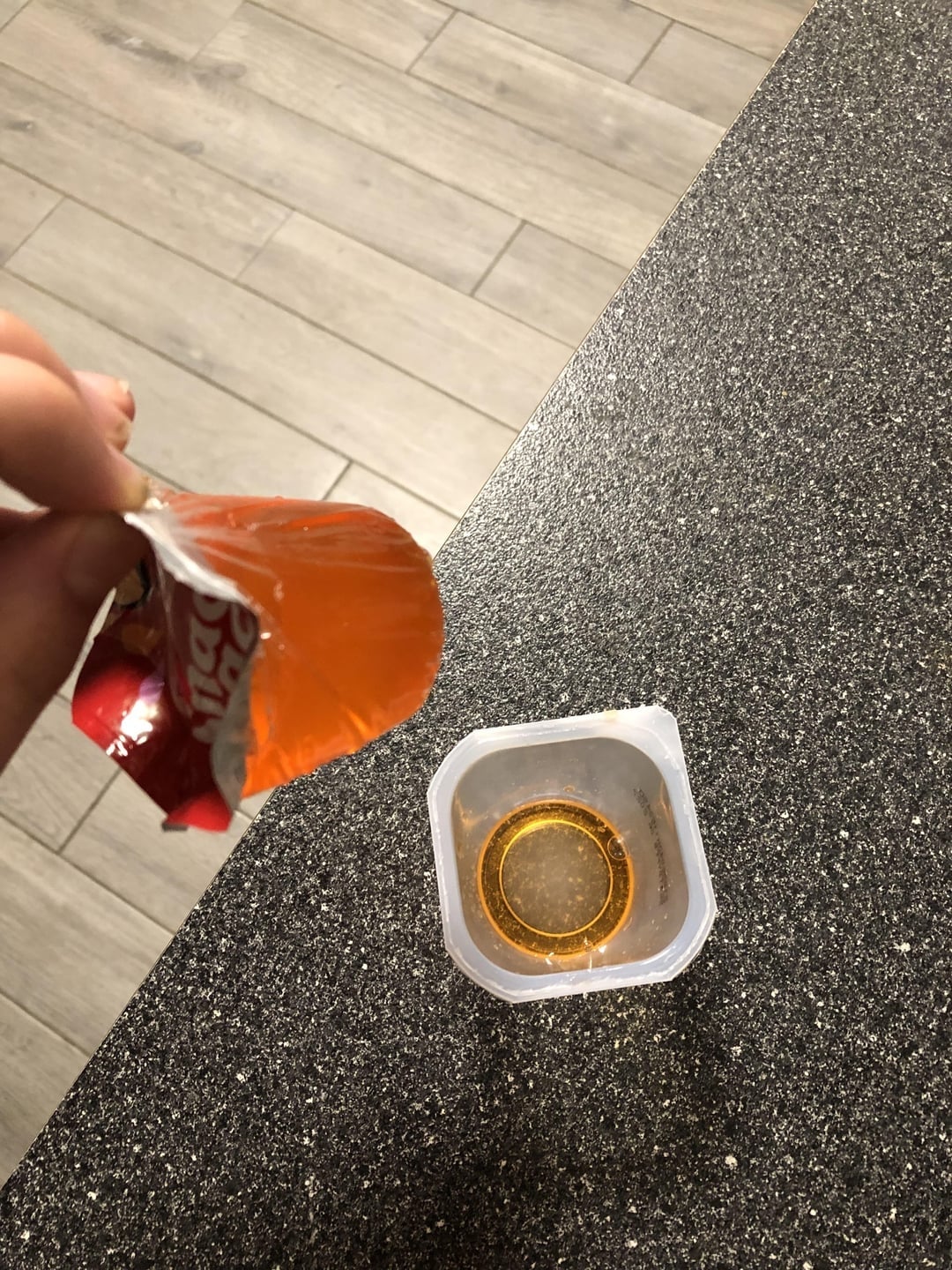 Peeled top of a single-serve applesauce container showing the empty peeled lid in one hand and the filled container on a countertop