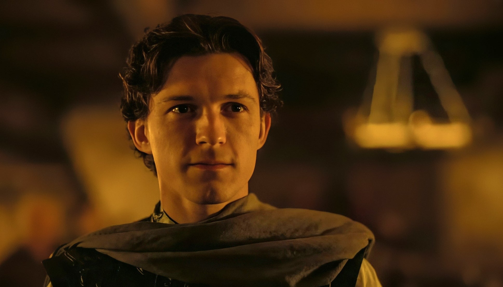 Person in medieval attire with a cloak, standing indoors with warm lighting