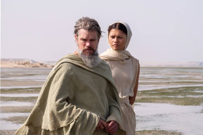 Two actors in ancient-style robes stand in a desert setting. One has a beard and long hair; the other wears a headscarf