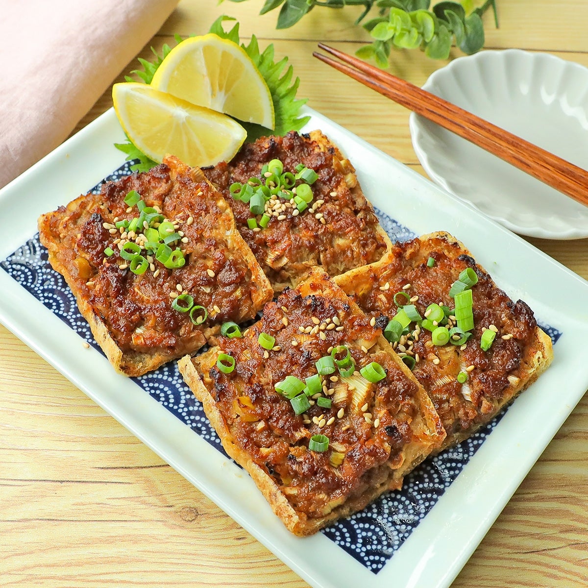 料理が盛られた皿に、ネギとゴマが載った油揚げ料理。そばにレモンと箸が置かれている。