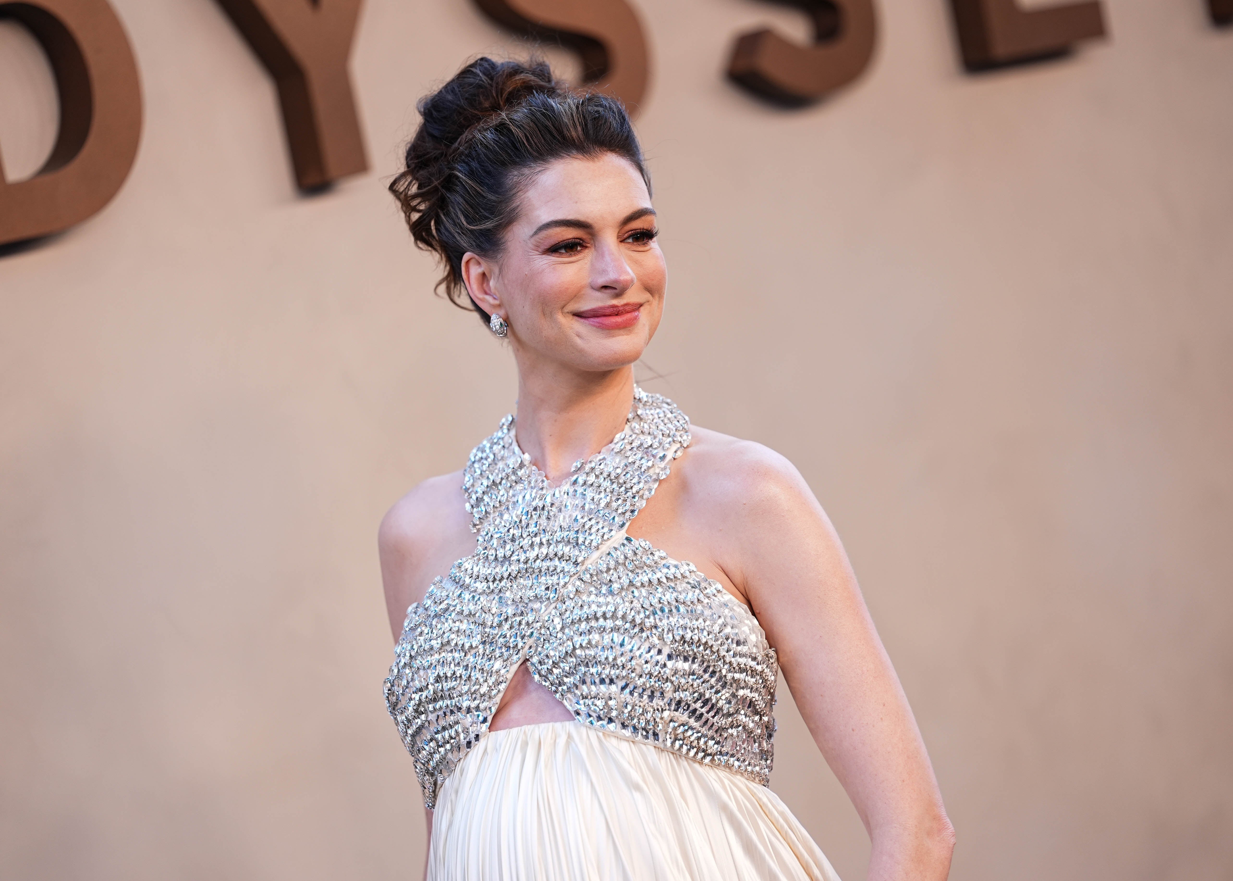 A person on a red carpet wearing an elegant, beaded halter dress with a pleated skirt, smiling and posing for photos