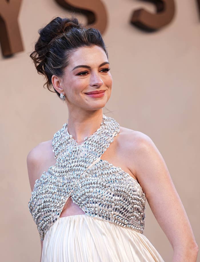 A person on a red carpet wearing an elegant, beaded halter dress with a pleated skirt, smiling and posing for photos
