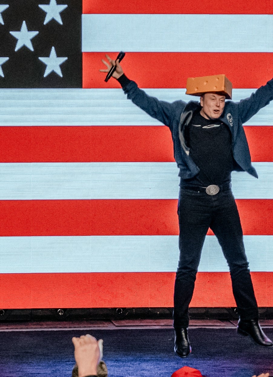 Performer on stage with arms raised in front of a large audience against a backdrop of the American flag. Two side panels read "VOTE."