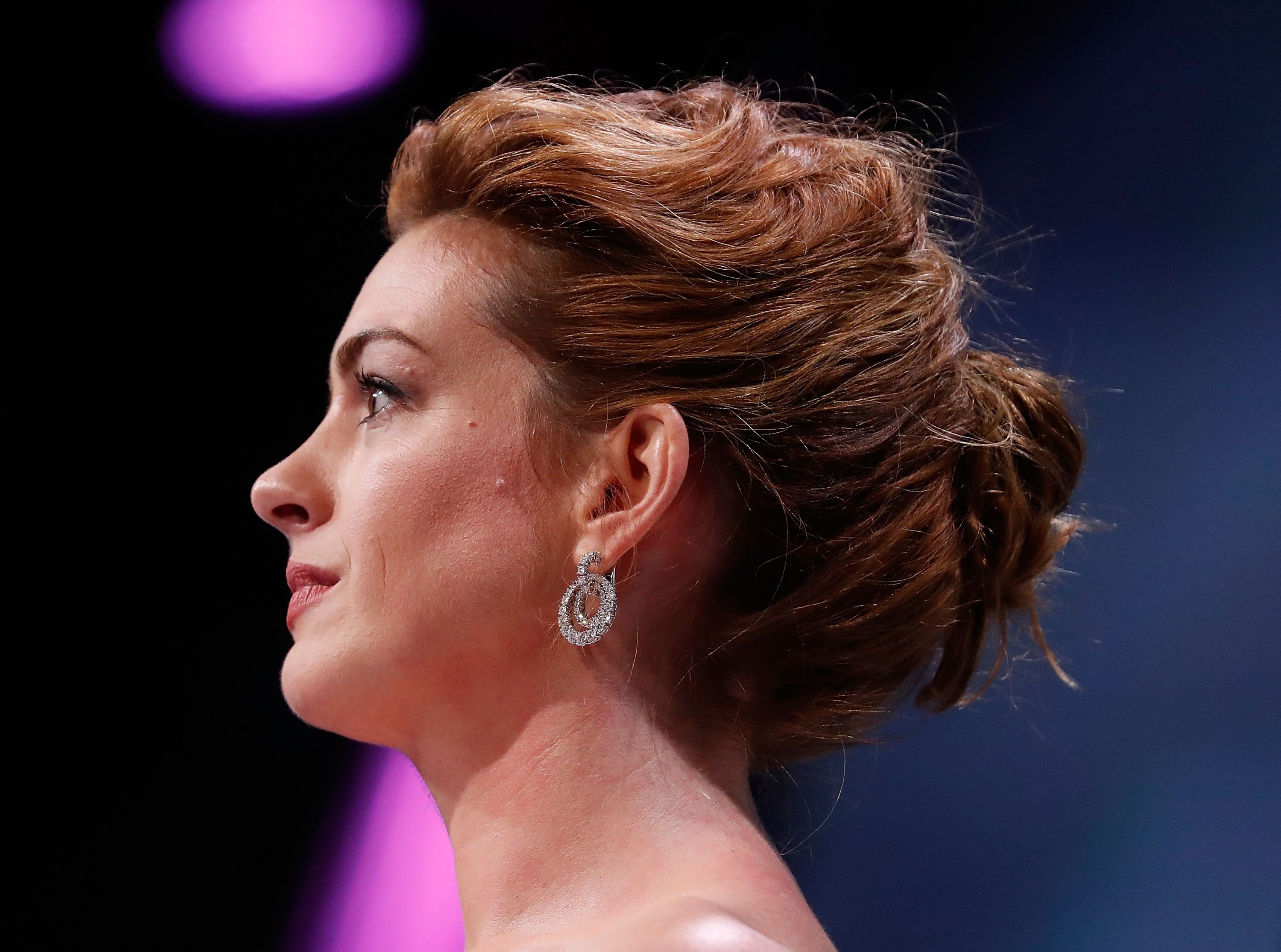 Woman with elegant updo hairstyle and dangling earrings, seen in profile under soft lighting