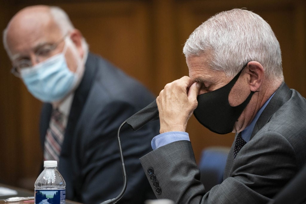 To personer i dress på et møte; den ene justerer briller under en maske, mens den andre lytter oppmerksomt