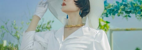 女性が大きな帽子と白い服を着て庭で空を見上げている写真。