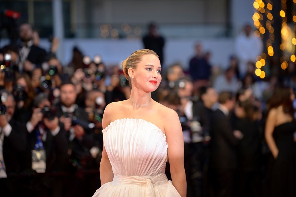 A person on a red carpet in a strapless, pleated gown, surrounded by photographers and onlookers