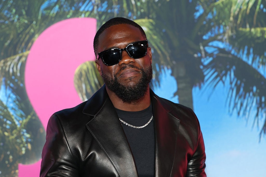 Man in sunglasses and a black leather jacket stands in front of palm trees at an event