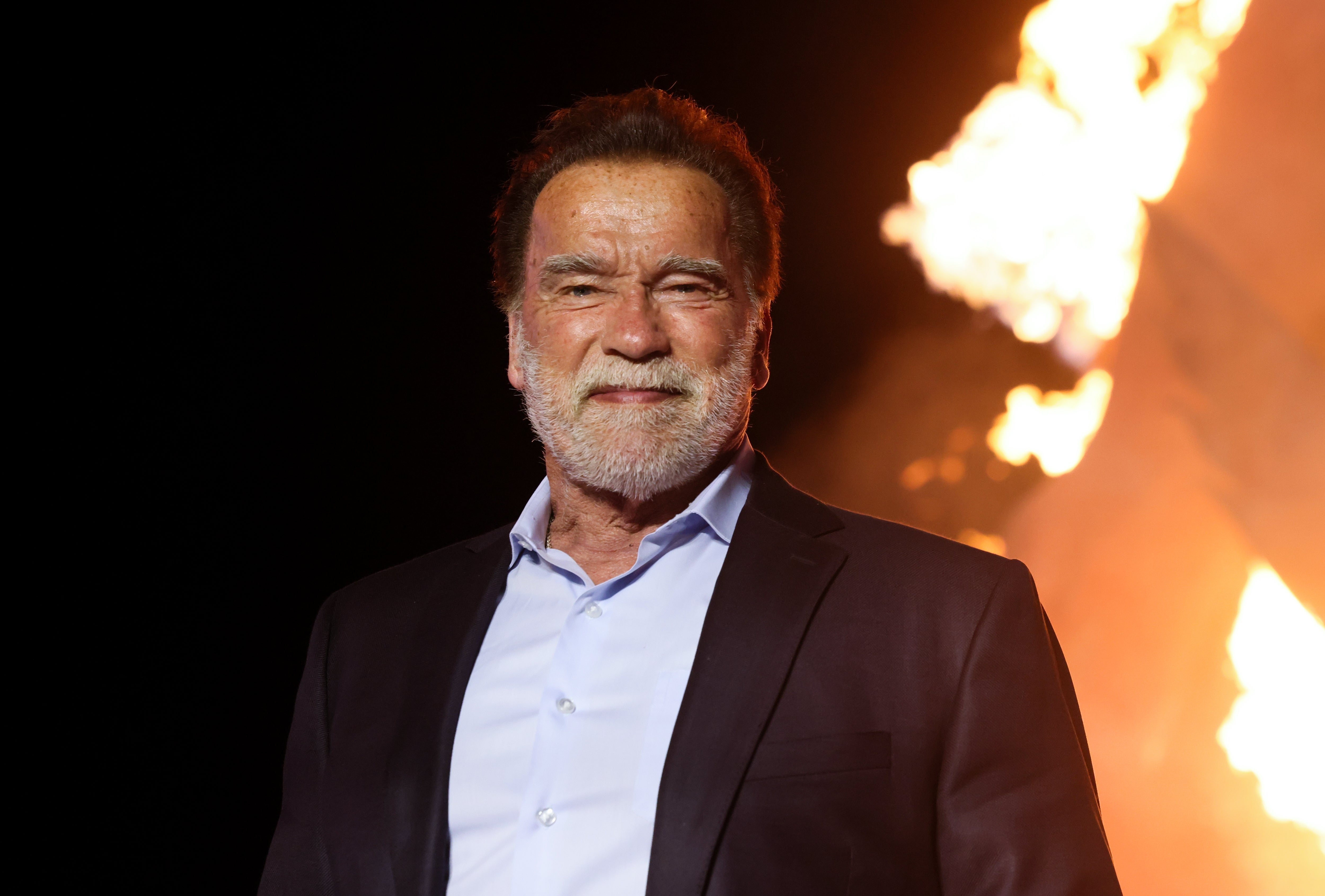 Man in a suit with a white shirt standing in front of a large fire background