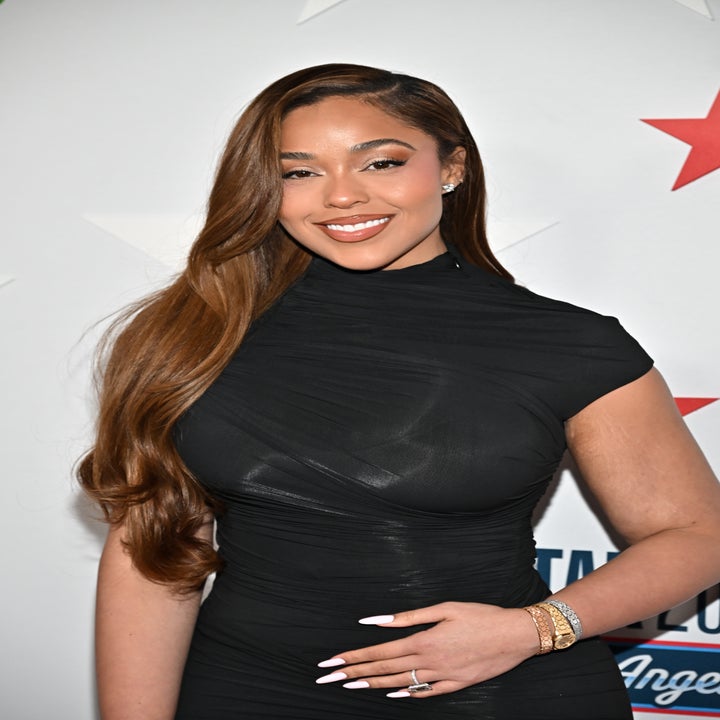 Person in elegant black dress at celebrity event, smiling with long hair draped over shoulder, wearing a bracelet and rings